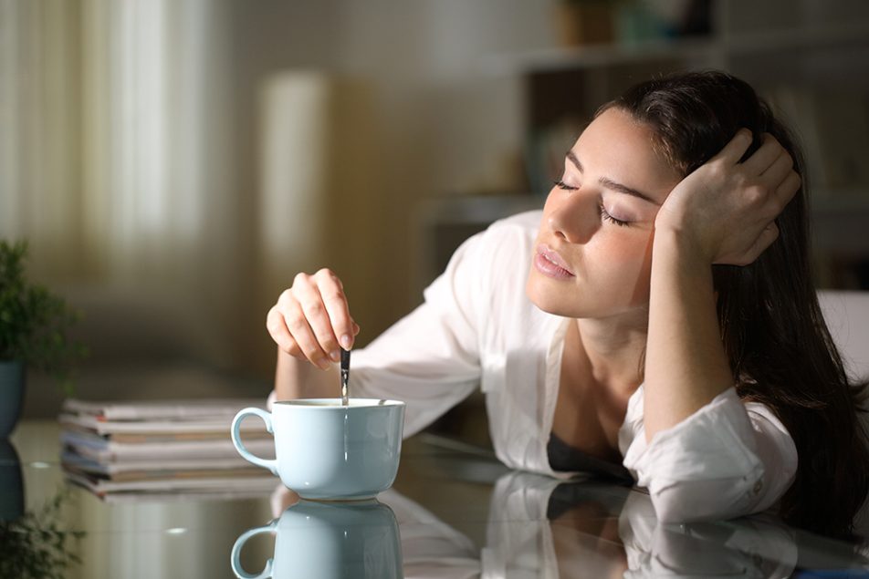 Al mattino, una donna mescola il caffè in cucina, mentre riflette sulle conseguenze psicologiche del dormire poco