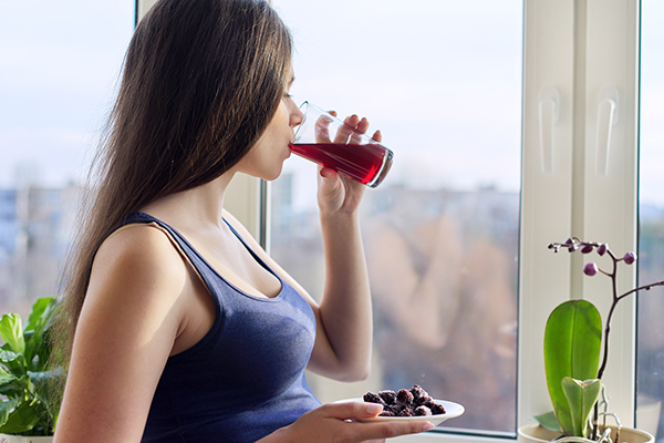 Giovane donna incinta che beve dal bicchiere un succo di mirtillo rosso fatto in casa, un esempio di cosa prendere in gravidanza contro la cistite