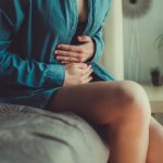 Donna seduta sul letto con le mani sull'addome a causa della cistite emorragica