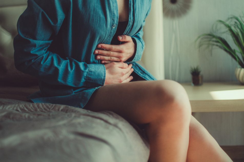 donna-che-soffre-di-cistite-emorragica Donna seduta sul letto con le mani sull'addome a causa della cistite emorragica