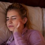 Donna a letto con sintomi del bruxismo mentre si tocca la mandibola dolorante