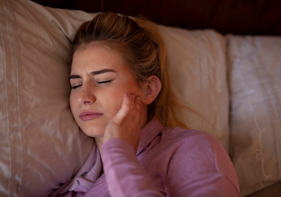 Donna a letto con sintomi del bruxismo mentre si tocca la mandibola dolorante
