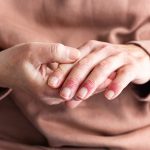Donna con dermatite atopica sulle mani si tocca le mani e i polpastrelli gonfi e arrossati