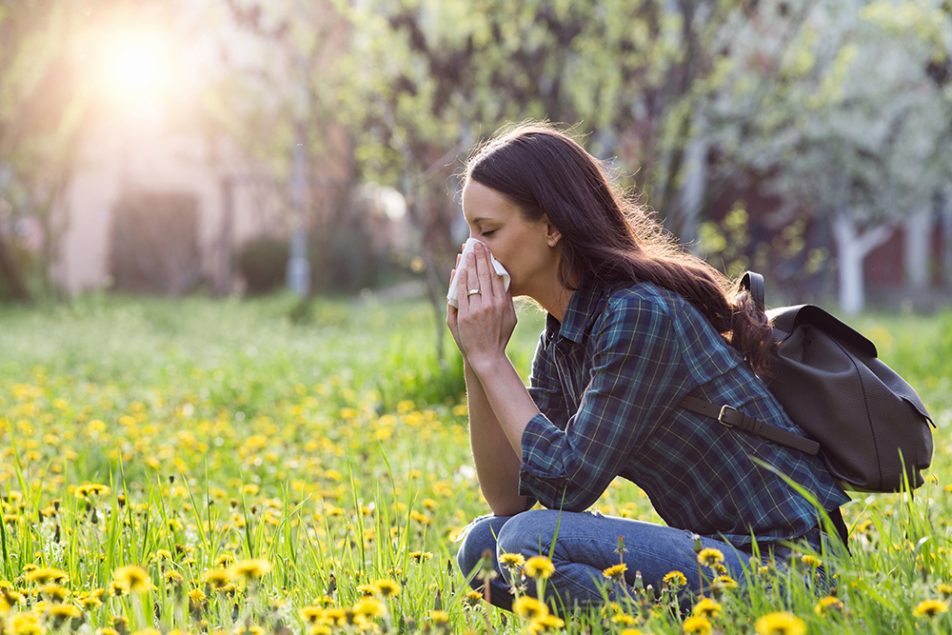 donna-con-rinite-allergica-su-prato-fiorito Donna che soffre di rinite allergica in un campo fiorito durante una passeggiata primaverile
