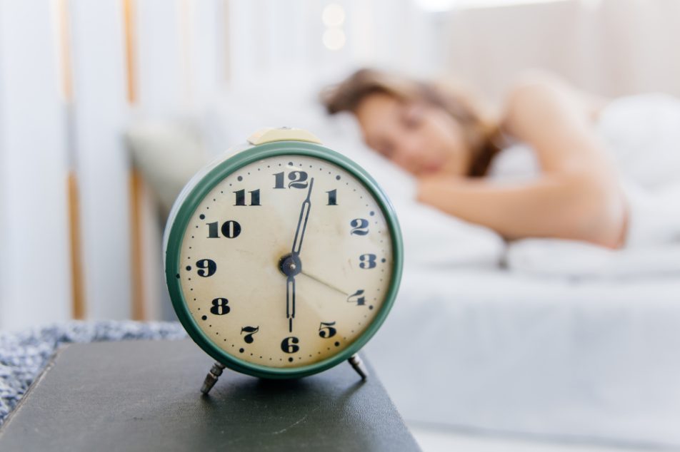 Sveglia in primo piano e donna con ritmo circadiano regolare che dorme nel suo letto