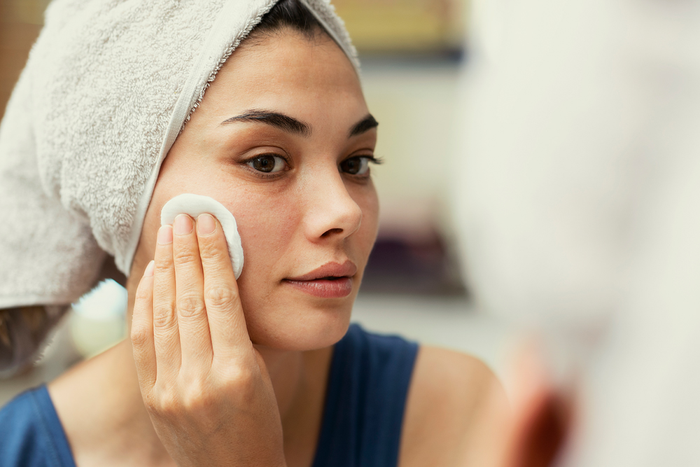 Giovane donna che deterge il viso dopo l’applicazione di una pasta di bicarbonato per il trattamento dei grani di miglio, in seguito a un consulto professionale