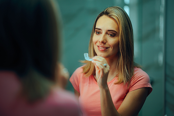 Donna in bagno davanti allo specchio, che affronta il digrignamento dei denti applicando un bite prima di andare a dormire