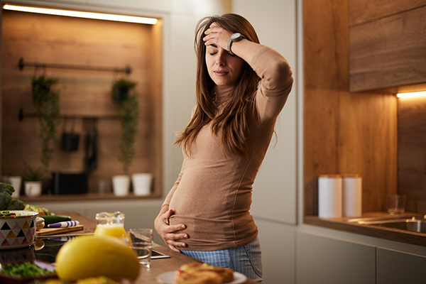 Donna in dolce attesa nella cucina di casa, che avverte stanchezza, dolore al basso ventre e altri sintomi dell’Escherichia coli mentre prepara un pasto