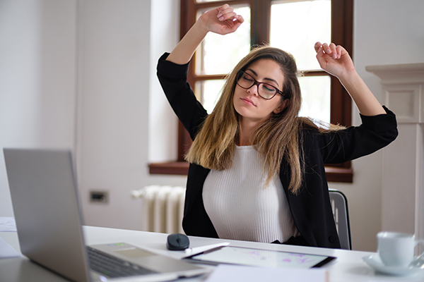 Donna che lavora in smart working soffre di insonnia e stress, e si stiracchia durante momento di pausa