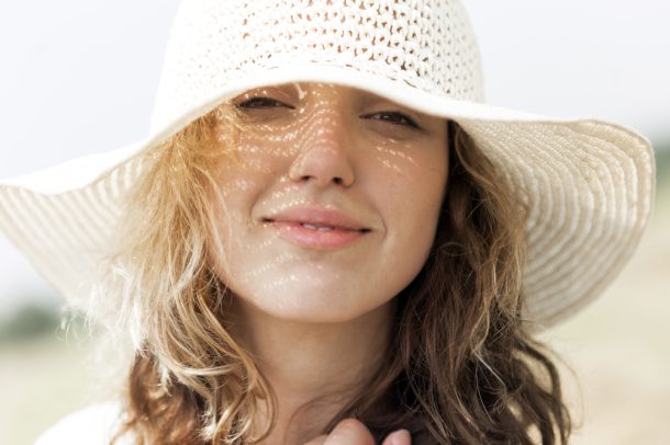 Giovane donna si protegge con un cappello per prevenire la macchie della pelle causate dal sole