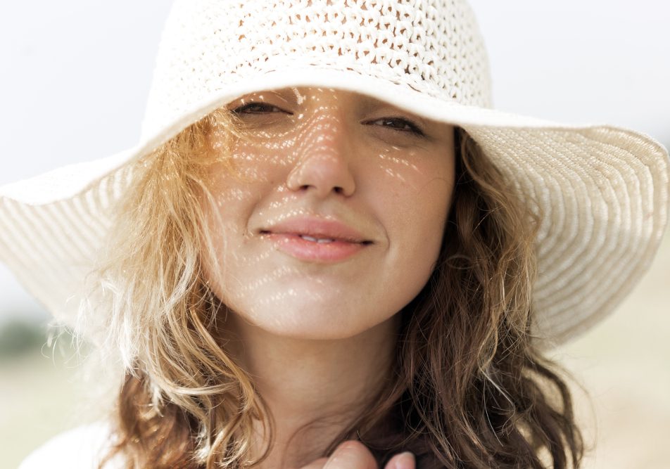 Giovane donna si protegge con un cappello per prevenire la macchie della pelle causate dal sole