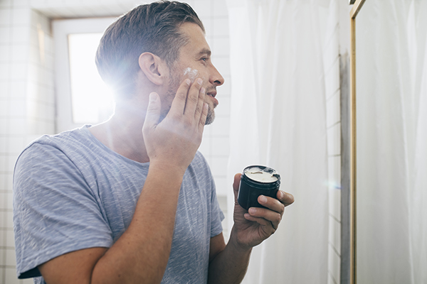 Giovane che, durante la sua routine mattutina, applica in bagno una crema per il viso per la cura della dermatite atopica