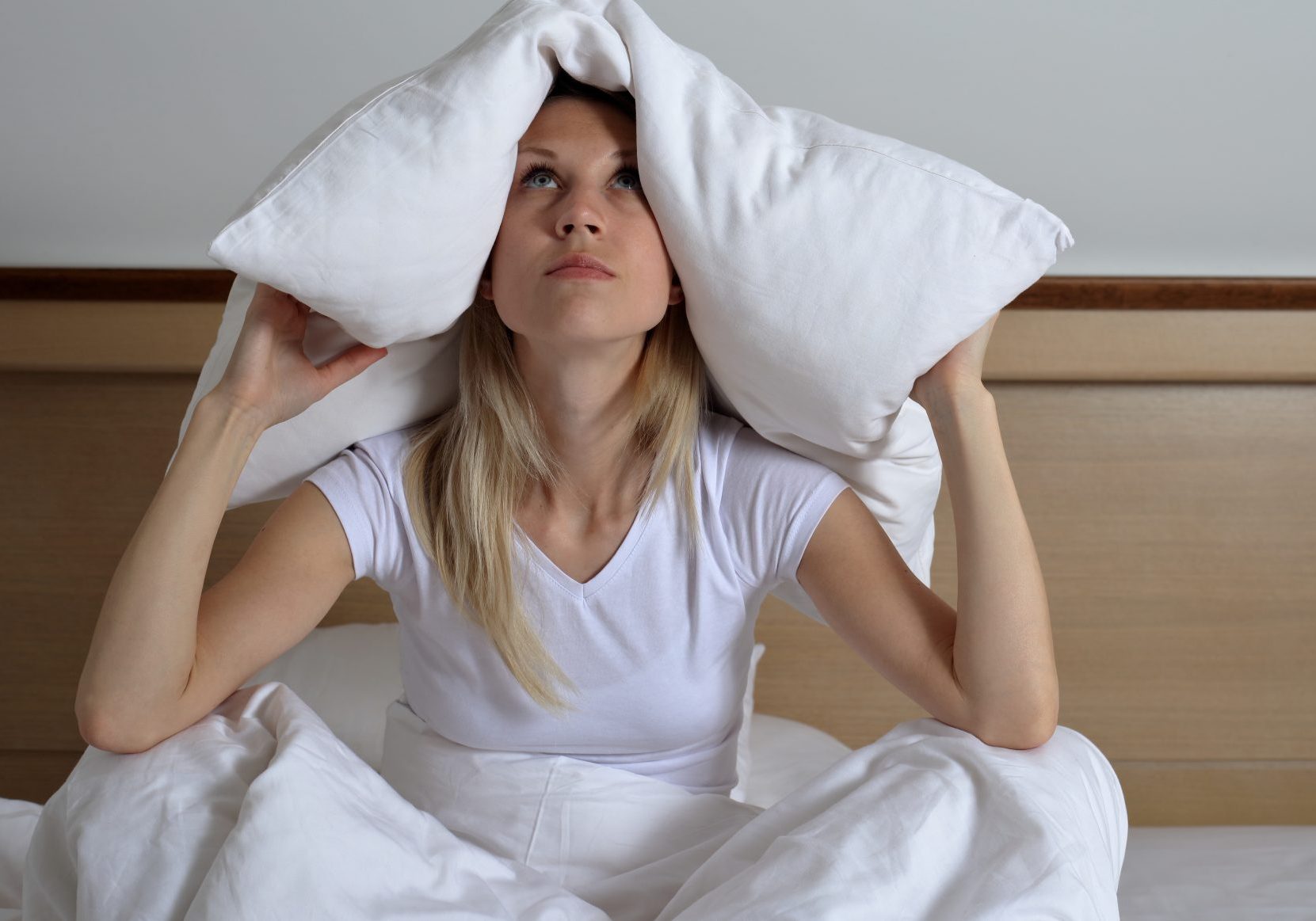 giovane-donna-che-soffre-di-disturbi-del-sonno Giovane donna seduta sul letto con cuscino sulla testa che soffre di disturbi del sonno