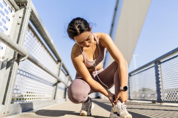 Giovane donna si tiene la caviglia per una distorsione durante la corsa