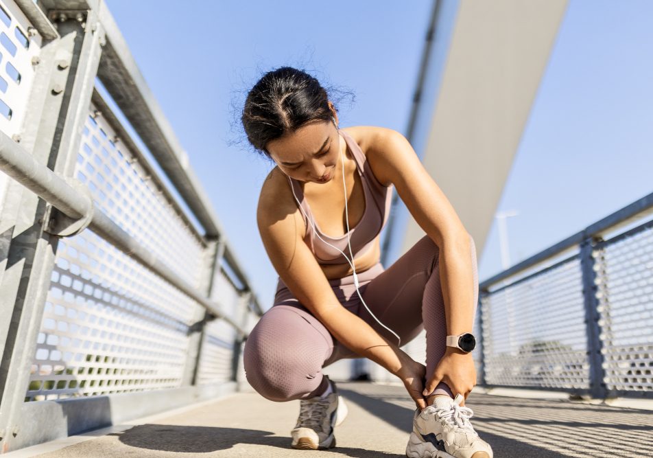 Giovane donna si tiene la caviglia per una distorsione durante la corsa