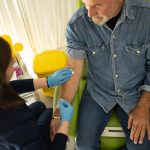 Infermiera che, mentre esegue il prelevo del sangue nel paziente maturo, gli illustra le cause dei trigliceridi alti e le possibilità di prevenzione