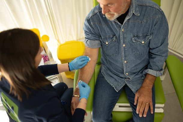 Infermiera che, mentre esegue il prelevo del sangue nel paziente maturo, gli illustra le cause dei trigliceridi alti e le possibilità di prevenzione