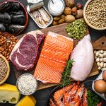 Tavola imbandita con alimenti ricchi di proteine, tra cui: pollo, legumi, formaggi, cozze e frutta secca