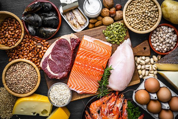 Tavola imbandita con alimenti ricchi di proteine, tra cui: pollo, legumi, formaggi, cozze e frutta secca