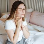 Giovane donna seduta sul letto con tosse da reflusso e mal di gola