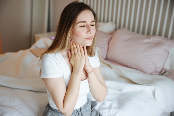 Giovane donna seduta sul letto con tosse da reflusso e mal di gola