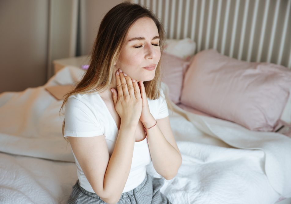 tosse-da-reflusso-mal-di-gola Giovane donna seduta sul letto con tosse da reflusso e mal di gola