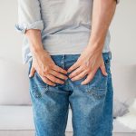 Uomo in jeans con una cisti pilonidale scoppiata che tiene le mani sulle natiche per attenuare il dolore