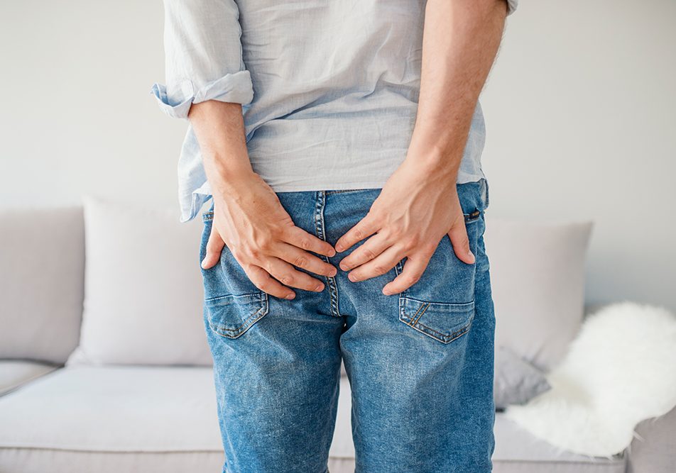 Uomo in jeans con una cisti pilonidale scoppiata che tiene le mani sulle natiche per attenuare il dolore