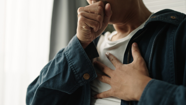 Uomo con tosse, tra i sintomi di tumore, si tocca il petto