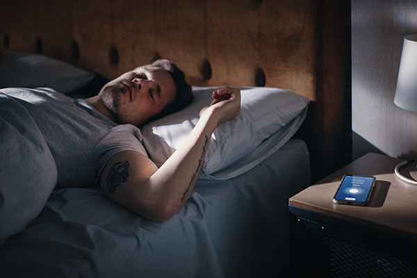 Uomo a letto che contrasta la sensazione di avere sempre sonno mantenendo orari costanti per dormire e svegliarsi