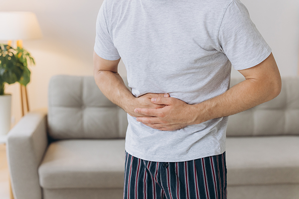 Uomo in comodo abbigliamento casalingo, davanti al divano, che avverte dolore addominale, uno dei sintomi dei trigliceridi alti
