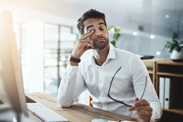 Uomo in ufficio seduto davanti al computer, che si sfrega gli occhi e si interroga sulle possibili cause della sua costante sonnolenza