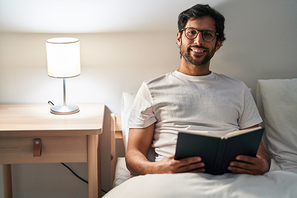 Uomo in camera da letto lieto di leggere un libro prima di coricarsi, uno dei possibili metodi per addormentarsi in serenità e rapidamente