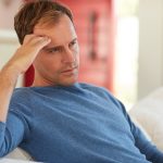 Uomo seduto sul divano che si tocca la fronte provocatogli da un’intensa cefalea, uno dei sintomi più comuni del tumore cerebrale