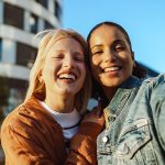 Amiche divertite che fanno un selfie durante una passeggiata in città, lungo la quale condividono informazioni su a cosa serve il progesterone e su altri temi di salute femminile
