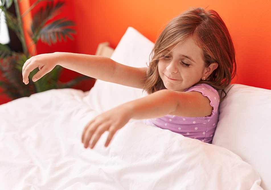 Bambina sorridente seduta sul letto che soffre di sonnambulismo, un disturbo del sonno comune in età infantile, e tiene le braccia alzate