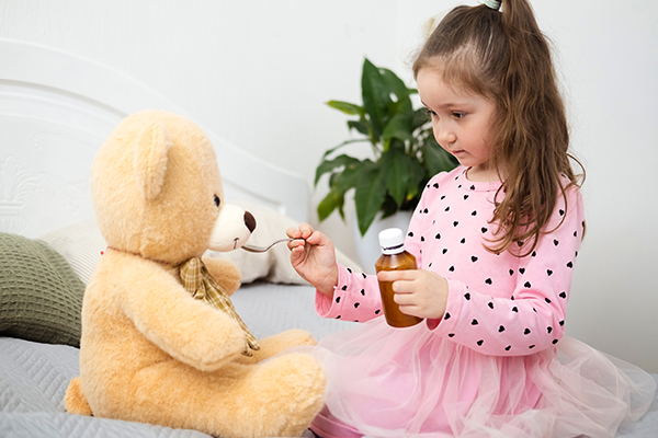 Bambina con addosso un vestito rosa che gioca a fare la dottoressa in casa e somministra delle gocce di betametasone al suo orsacchiotto