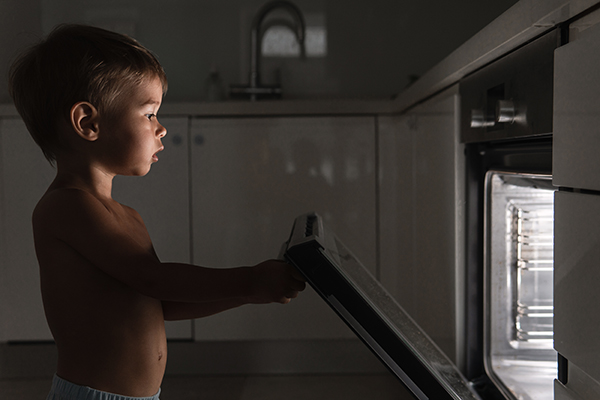 Bambino curioso che soffre di sonnambulismo a occhi aperti mentre apre il forno elettrico durante una notte movimentata