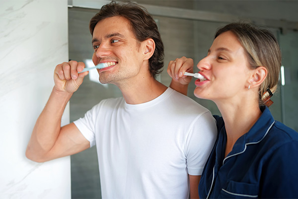 Coppia affiatata in bagno, davanti allo specchio, che lava e risciacqua i denti usando acqua salata in seguito all’estrazione del dente del giudizio