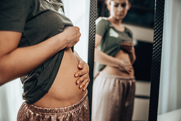 Donna davanti allo specchio che osserva gli effetti del progesterone sul corpo, in particolare nella zona addominale