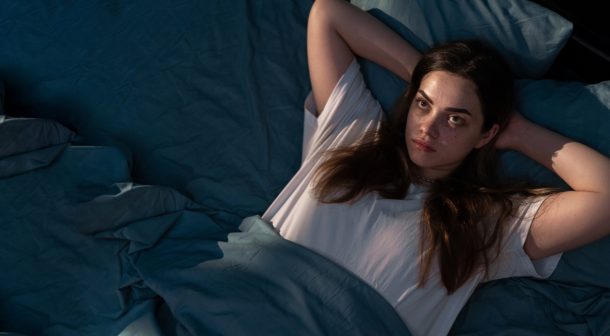 Giovane donna a letto che ha difficoltà a rilassarsi, tra i sintomi fisici dell'ansia notturna