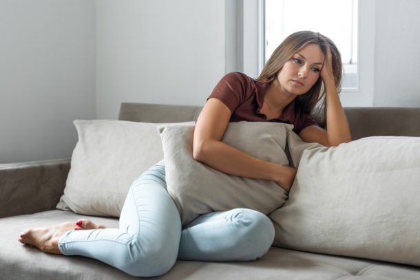 Donna seduta sul divano mostra sofferenza pe la nausea da ansia