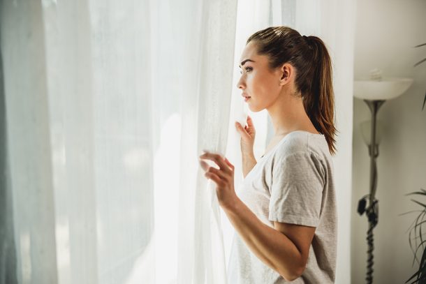 Donna apprensiva, con sintomi di ansia e depressione, che guarda fuori dalla finestra del salotto di casa