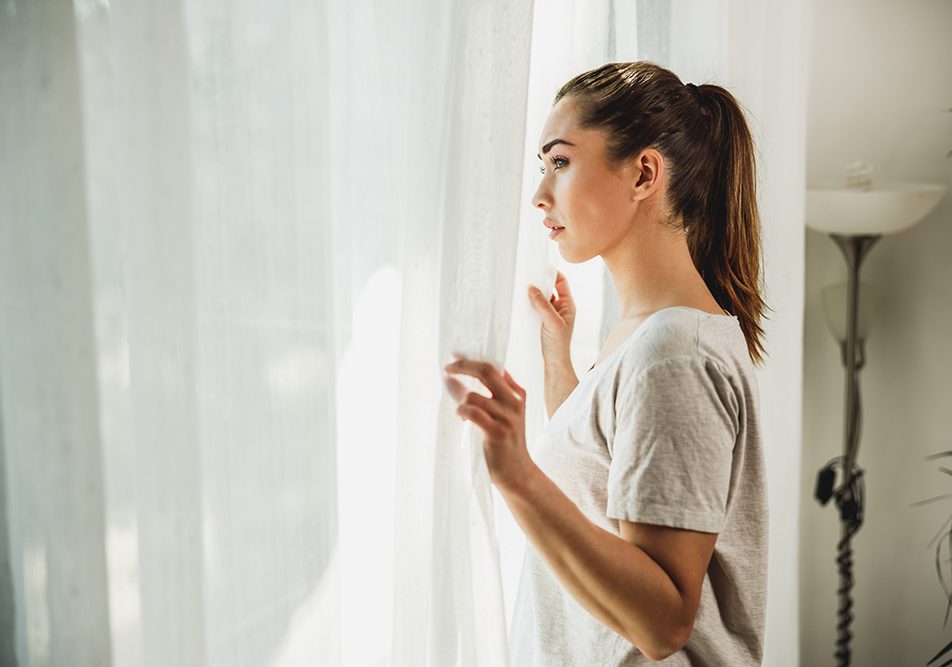 donna-con-ansia-e-depressione-sintomi-guardando-fuori-dalla-finestra Donna apprensiva, con sintomi di ansia e depressione, che guarda fuori dalla finestra del salotto di casa