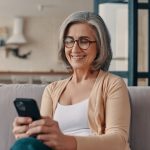 Donna matura sul suo divano guardando cellulare che soffre di cisti renali asintomatiche