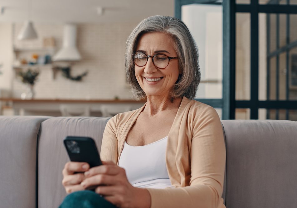 Donna matura sul suo divano guardando cellulare che soffre di cisti renali asintomatiche