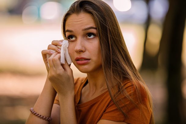 donna-con-congiuntivite-allergica-strofinando-occhi Donna al parco con una congiuntivite allergica che strofina gli occhi lacrimanti usando un fazzoletto