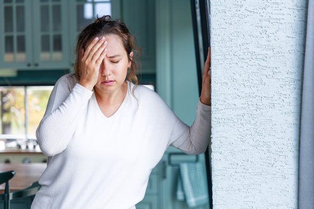 donna-con-crisi-epilettiche-sintomi-toccandosi-fronte-e-appoggiandosi-al-muro Donna in cucina che sperimenta sintomi di una crisi epilettica mentre si tocca la fronte e appoggia il palmo della mano al muro