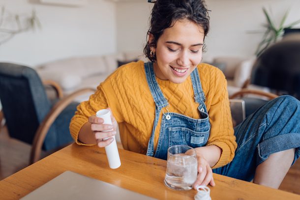 donna-con-eczema-assumendo-compressa-a-base-di-cortisone Giovane donna che soffre di eczema mentre assume una compressa effervescente a base di cortisone nel soggiorno di casa