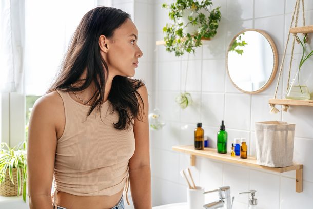 Donna con perdite durante l’ovulazione che guarda il suo riflesso allo specchio del bagno mentre cerca una soluzione al suo problema di salute